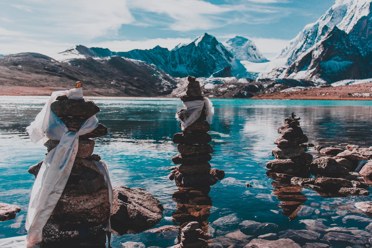 about-01 Calm lake scene with majestic snow-capped mountains and tranquil rock cairns.